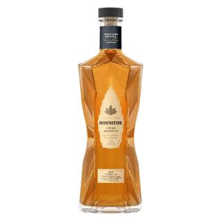 A bottle of Hornitos Ancho Reserve tequila on a solid white background. The bottle is faceted to show the amber-colored liquid inside, featuring a cream-colored label with a green hornitos leaf logo and a black cap.