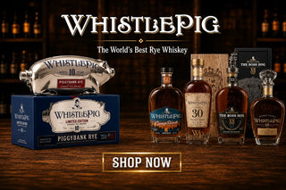 WhistlePig whiskey bottles and packaging on a wooden surface with a dark background.